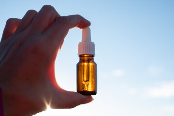Essential oil bottle in hand against sunny sky. Little brown medicine bottle in nature background....