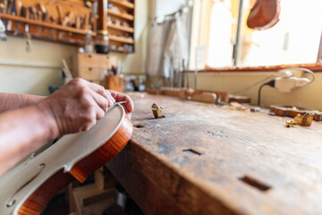 luthier carving the shape of the outside of the front of a violin with gouge