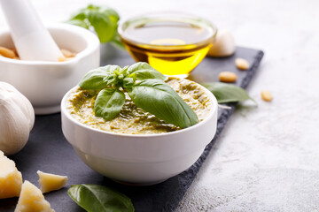 Pesto sauce and ingredients, black cheese board, basil, garlic, pine nuts, olive oil on grey stone background with copy space