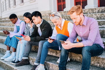 Group of teenegers browsing with the smartphones sitting together outdoors.