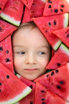 The face of a child in a frame of watermelon slices.Red berry pulp.A boy framed by triangular pieces of watermelon.Funny summer picture.Cute portrait of a baby.Child with watermelon