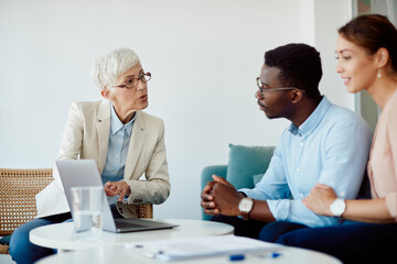 Senior financial advisor using laptop while talking to young couple during meeting in office.