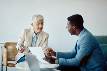 Obraz premium Senior businesswoman and her young her colleague talk while going through paperwork in office.