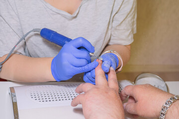 Manicurist master removing cuticles. Processing of rough cuticles and lateral folds of male nails on hands with a conical instrument. Medical hardware manicure in a beauty salon