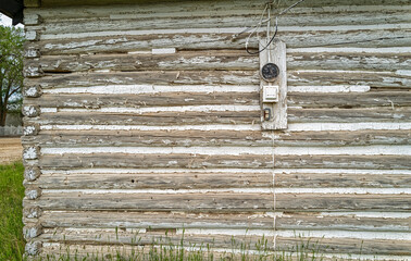 Electric meter and conduits on the exterior wall of an old log building