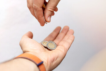 Close up of male hand putting coin into another hand, donation.