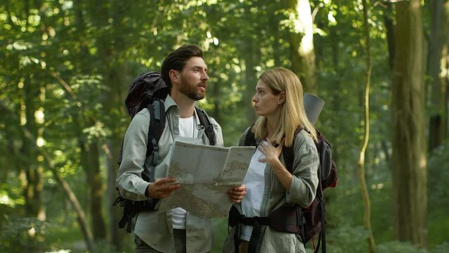 Emotional man and woman tourists getting lost in forest, arguing with map, feeling disagree, go in different directions