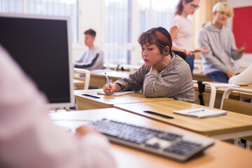 Portrait of tired or bored teenage female pupil sitting at desk in classroom during lesson