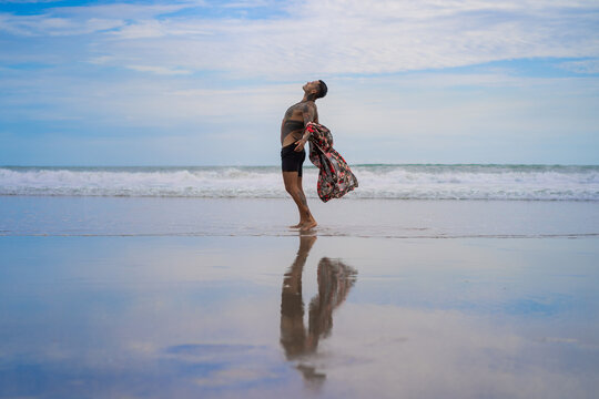 Handsome tanned tattooed sexy man with a naked torso in a flying poreo on the ocean at sunset.