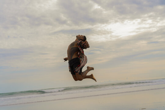 Handsome tanned tattooed sexy man with a naked torso in a flying poreo on the ocean at sunset.