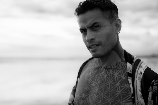 Handsome tanned tattooed sexy man with a naked torso in a flying poreo on the ocean at sunset.