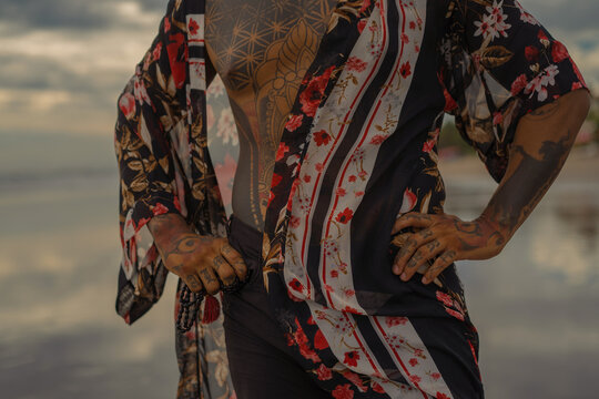 Handsome tanned tattooed sexy man with a naked torso in a flying poreo on the ocean at sunset.