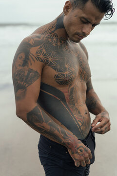 Handsome tanned tattooed sexy man with a naked torso in a flying poreo on the ocean at sunset.