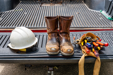 A electrician took his old worn boots, hard hat and tool belt off and put them on a pickup truck tail gate.
