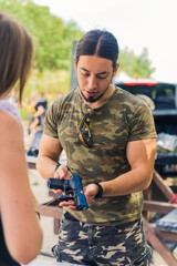 Caucasian muscular man wearing camo t-shirt presenting a handgun to female client. Buying and...
