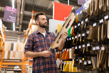 male shopper in a hardware store chooses a large spatula for wall plastering