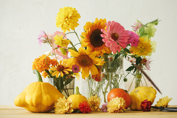 Stylish autumn composition on rustic table. Colorful autumn flowers, pumpkins, pattypan squashes on wooden table in atmospheric room. Harvest in countryside. Happy Thanksgiving! Hello Fall