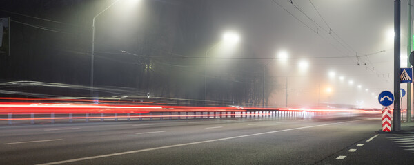 View empty dark night blue foggy misty rainy highway city road backlight red traces low poor visibility cold spring autumn season. Seasonal bad rainy weather accident danger warning car fog light