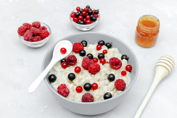 Oatmeal porridge with summer raspberry, currant berries,honey. Porridge oats in bowl with fruits. Healthy food breakfast,lifestyle,dieting, proper nutrition.Top view flat lay on gray table background