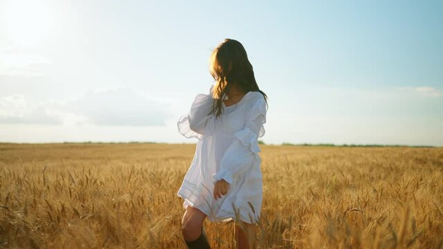happy young woman in white dress with string bag with bread is whirling in rye field in summer sunny day