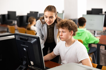 Obraz premium Female teacher and her student, teenage boy, looking at monitor of PC during computer science lesson.