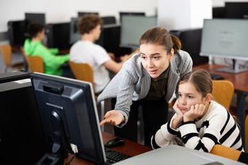 Teacher helping sad young girl to solve computer problem during lesson.