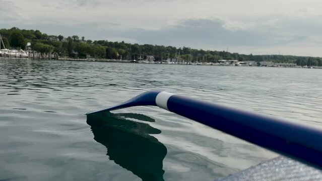 Stunning lake views from the point of view of a paddle board. Blue paddle board oar is skimming the waters surface. The paddle ebbs and flows with the movement of the water. Views of the shoreline.