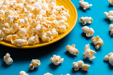 Popcorn on a yellow plate on blue background, Food or snack, Health or salt