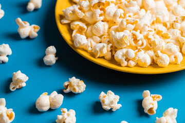 Popcorn on a yellow plate on blue background, Food or snack, Health or salt