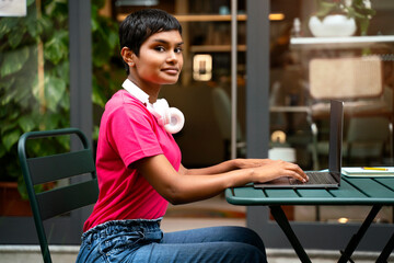 Portrait of Indian woman using laptop computer, typing, working freelance project looking at camera...