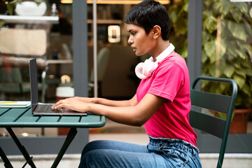 Fototapeta na wymiar Pensive asian woman freelancer using laptop computer typing working online sitting at workplace. Stylish Indian student studying, distance learning, education concept 