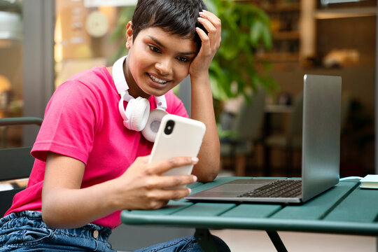 Smiling Indian woman using mobile phone, reading text message sitting outdoors. Asian freelancer working online sitting at workplace 