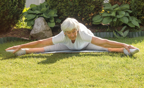 an aged elderly gray-haired woman does therapeutic exercises for stretching muscles and hip joints. exercise splits, yoga asana. High quality photo
