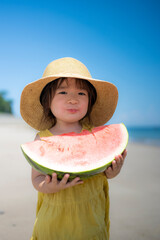 夏の海の砂浜でスイカを食べる2歳の女の子