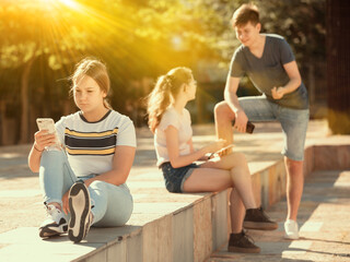 Obraz premium Teen girl sitting with phone separately on summer city street. Concept of lack of real communication among adolescents
