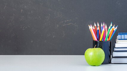 Back to school background with colored pencils, books and apple on a desk in classroom with copy...