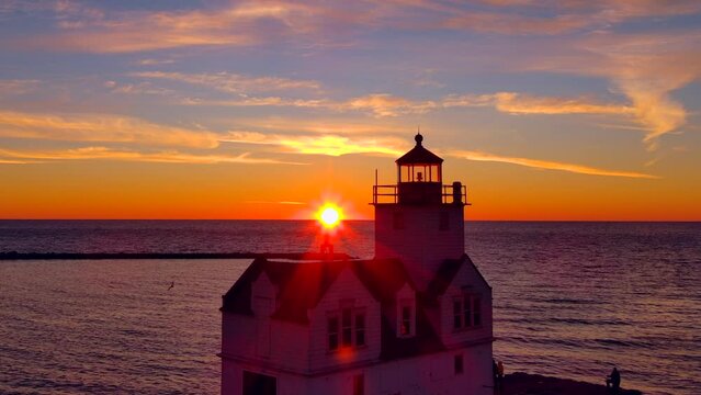 Incredible sunrise sky over lighthouse, drones flying and filming. Silhouetted people fishing.
