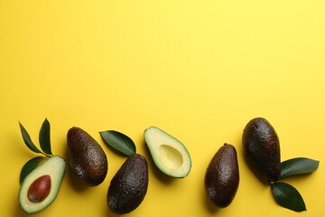 Whole and cut ripe avocadoes with green leaves on yellow background, flat lay. Space for text