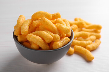 Many tasty cheesy corn puffs on white wooden table, closeup