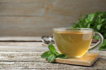 Cup of hot aromatic mint tea on wooden table. Space for text