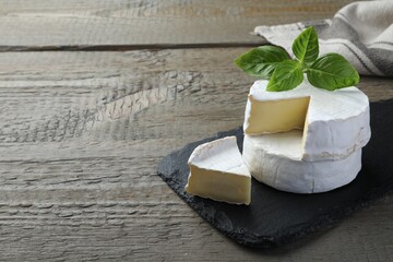 Tasty cut and whole brie cheeses with basil on wooden table, space for text