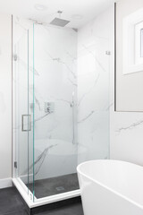 A freestanding tub and a marble lined shower with glass walls and chrome faucet.