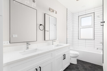 A white luxury bathroom with a white vanity cabinet and marble countertop, subway tile shower, and...