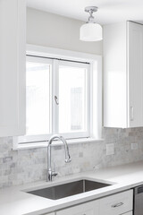 A kitchen sink detail shot with white cabinets, a marble subway tile backsplash, and a light hanging above the window.