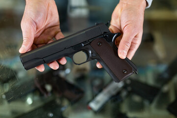 Pair of hands holding pistol over showcase in arms shop.
