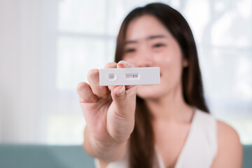 Asian woman showing rapid antigen test kit for selftest with Negative result during swab COVID-19 testing, female holding perform self in living room at home