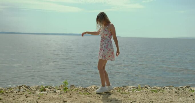 Shuffle dance, a girl dances on the seashore, in white sneakers and a white sundress.