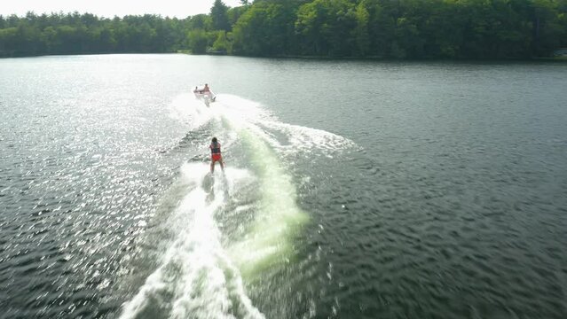 Outdoor shot of a woman water skiing outside in a blue lake With many luscious, green trees in the background and a cloudy sky, a splash of water or waves can be observed. USA