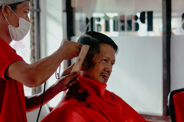 The barber man is cutting the old man's hair
