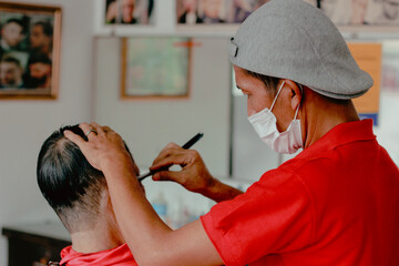 The barber man is cutting the old man's hair
